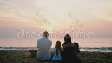 后景幸福一家四口坐在一起观看海浪在惊人的热带日落海洋海滩与史诗般的天空。